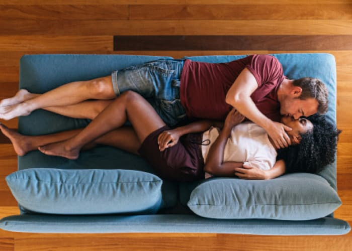 happy multiethnic lovers resting on sofa and kissing at home