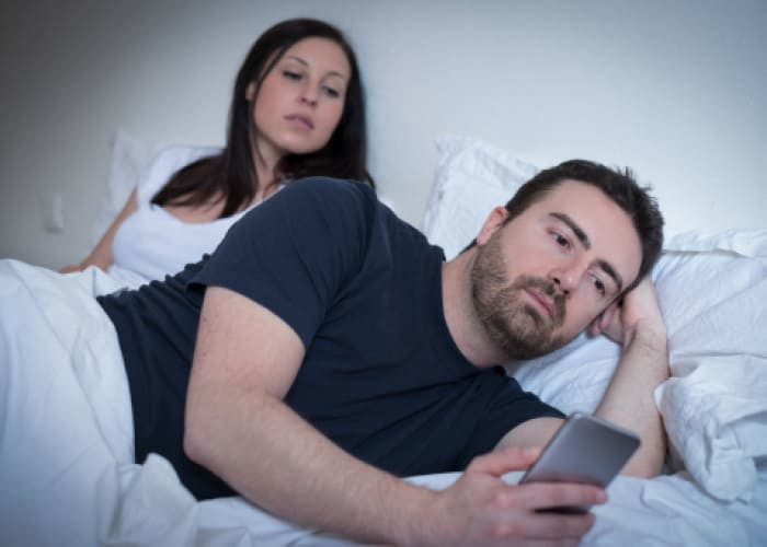 man neglecting his girlfriend and using his mobile phone in bed