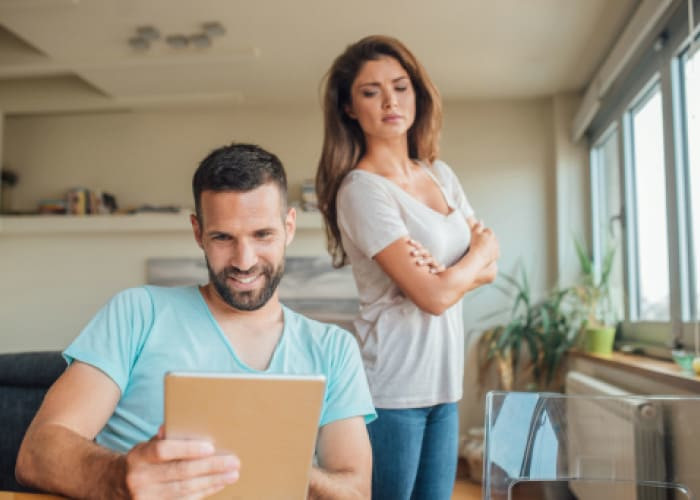 young woman jealously looking at the smiling man using digital tablet			