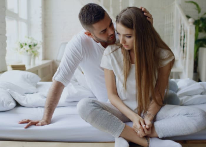 depressed young woman sitting in bed and crying while her boylfriend come and embrace