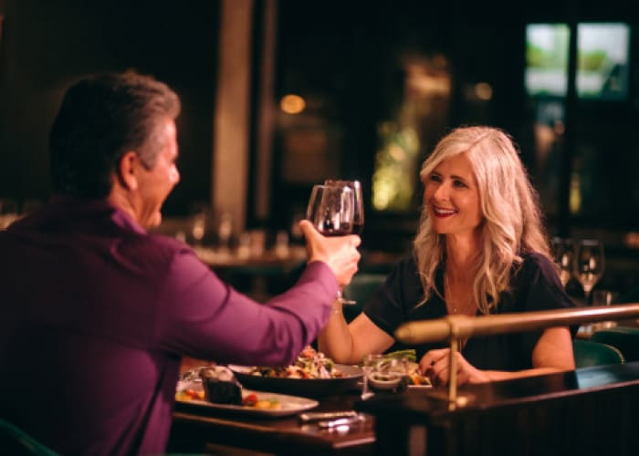 smiling mature husband and wife toasting with wine at dinner		