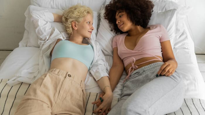 multiracial lesbian couple holding hands while lying on bed at home